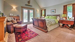 Ein Schlafzimmer mit einem großen Bett, einem hölzernen Schminktisch, einem Ledersessel und einem roten Teppich mit Muster.