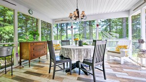 Ein überdachter Balkon mit Tisch und Stühlen, umgeben von großen Fenstern mit Blick auf einen Wald.