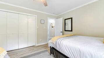 A bedroom with a bed, a ceiling fan, a wardrobe, and a door leading to another room.