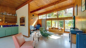 A spacious living area with a wooden ceiling, large windows, a green armchair, a pink sofa, and a kitchen with wooden cabinets and a blue countertop. - 2 Mi to Riverwalk: Palmetto Gem w/ Fire Pit & BBQ (Palmetto)