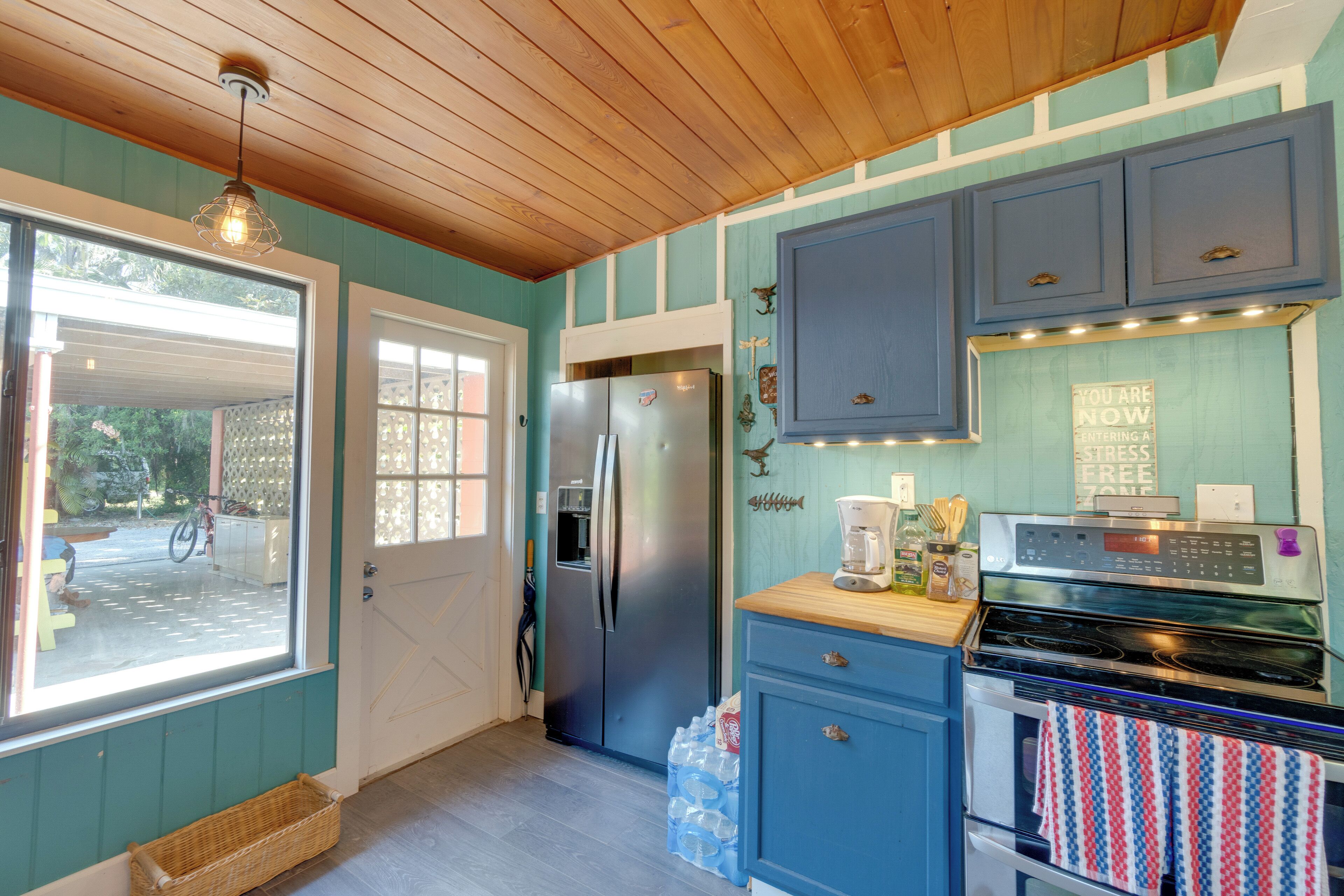 A kitchen with teal walls, wooden ceiling, stainless steel appliances, and a view through a window.