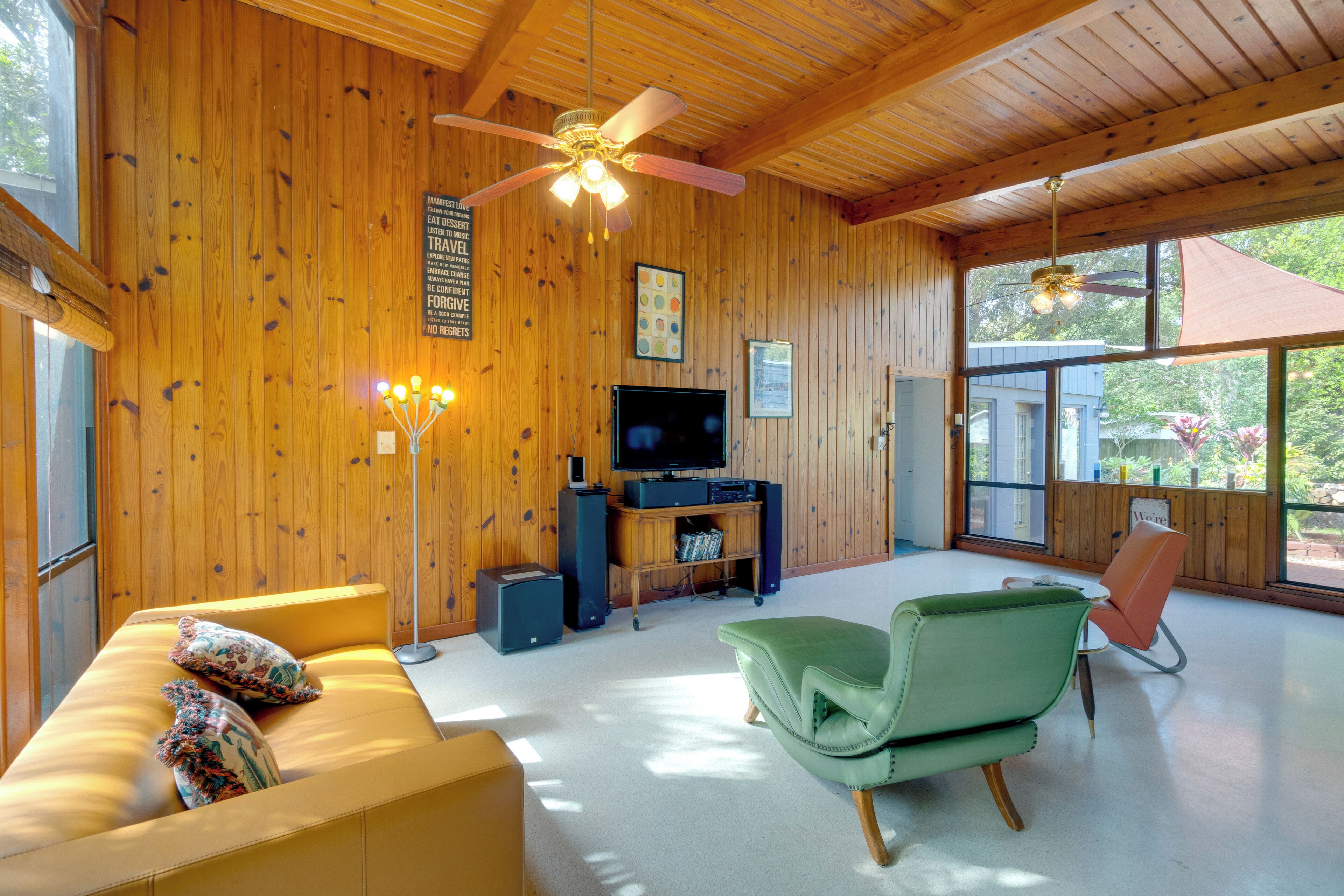 Una sala de estar acogedora con paredes de madera, un ventilador de techo, un televisor de pantalla plana, un sofá y un sillón verde.