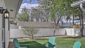 A patio with two green Adirondack chairs, a string of lights, and a white fence in the background. - Pet-friendly Canon City Home w/ Fenced Yard! (Canon City)