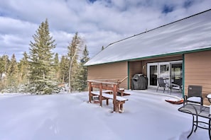 Une terrasse en bois avec un banc et une table, entourée d’un paysage enneigé et d’arbres.