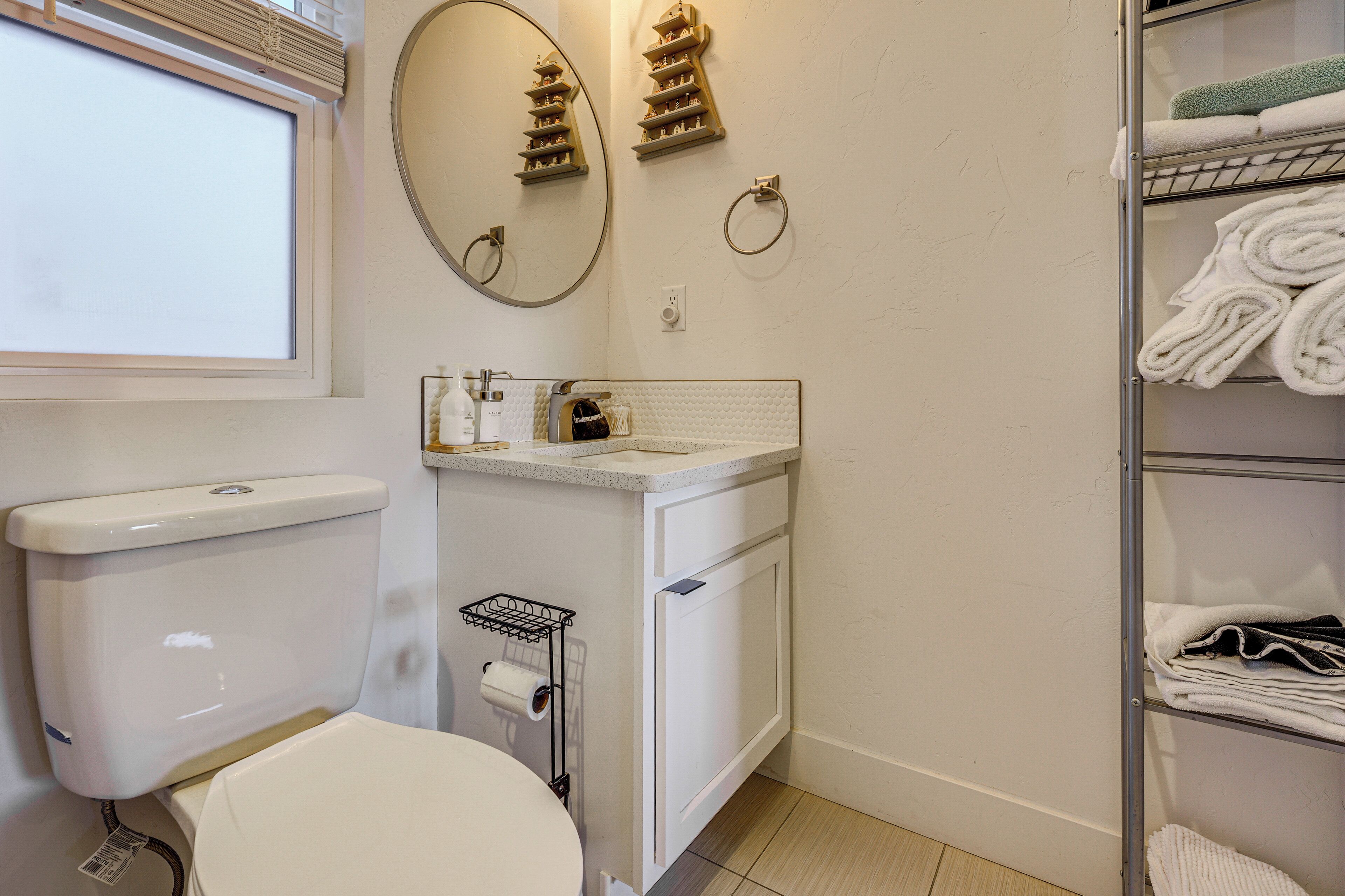 A bathroom with a toilet, sink, mirror, towel rack, and a shelf with folded towels.
