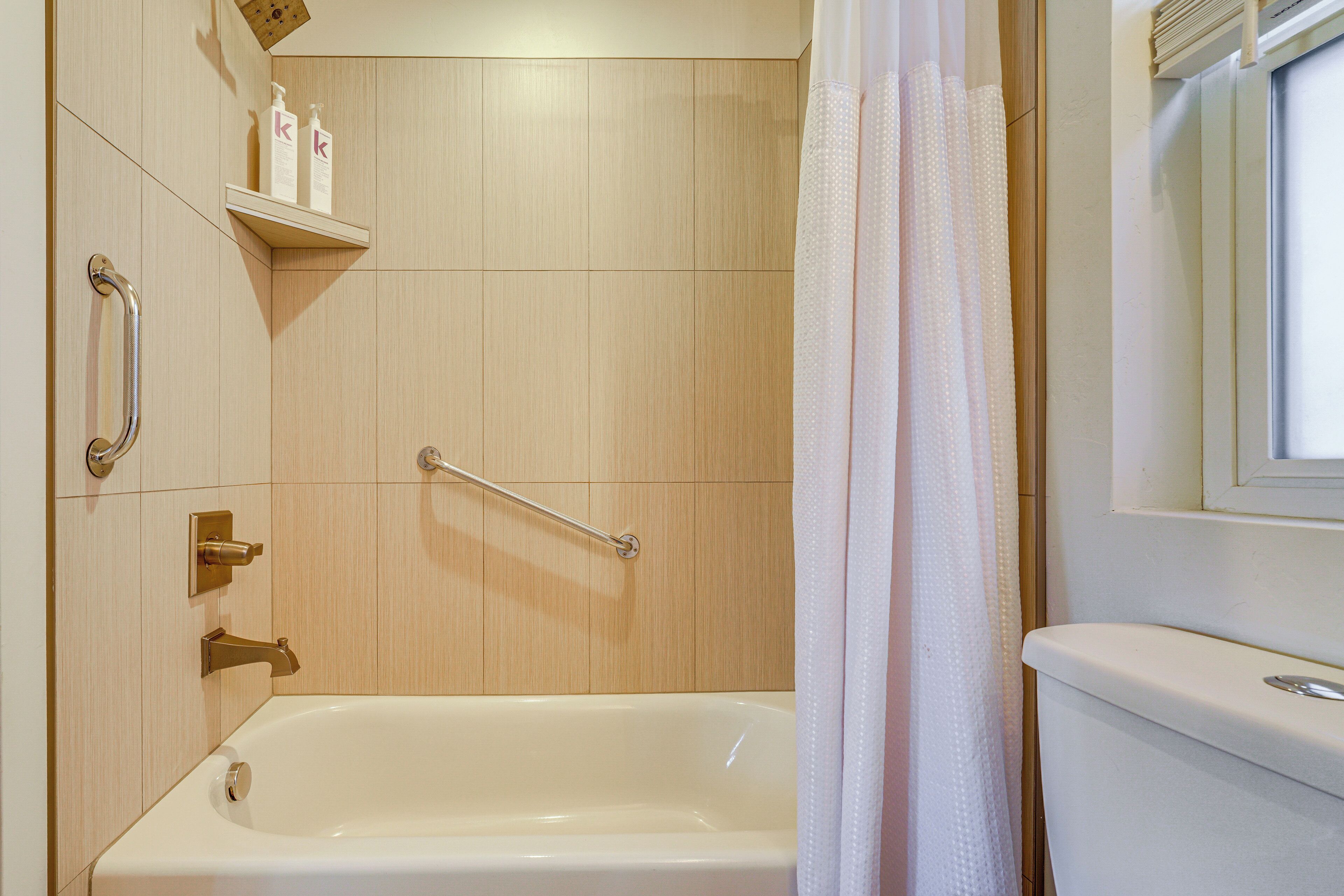 A bathroom with a bathtub, a shower with a grab bar, and a toilet.
