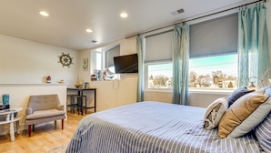 A bedroom with a large bed, a desk, a chair, a television, and a view of the outside. - Dtwn Walkability! Grand Junction Couple's Retreat (Grand Junction)