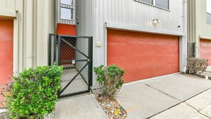 Um edifício moderno com porta de garagem, portão fechado e pequenos arbustos.