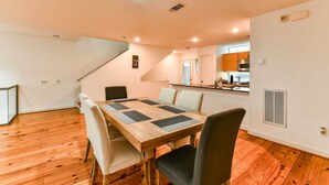 Uma área de refeições com mesa de madeira, quatro cadeiras e uma cozinha ao fundo.