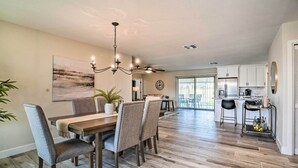 A spacious dining area with a wooden table and chairs, a chandelier, and a view into the kitchen.