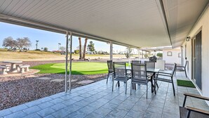 A covered patio with a view of a golf course, outdoor seating, and a small garden area.