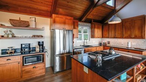 A modern kitchen with wooden cabinets, a stainless steel refrigerator, a built-in oven, and a large island with a black countertop. - Hot Tub + Ocean Views: Spacious Irish Beach Home! (Manchester)