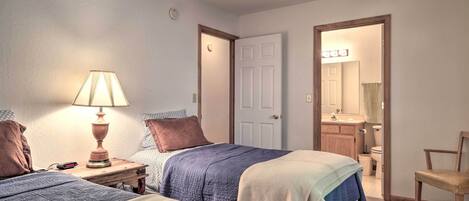 A bedroom with two beds, a nightstand with a lamp, a chair, and a bathroom visible through an open door.