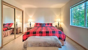 A bedroom with a large bed, two bedside lamps, a mirror, and a window with a view of trees.