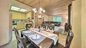 A dining area with a long table set for six, a chandelier, and a view of a living room with a fireplace.
