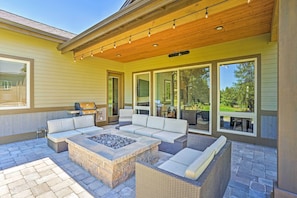 An outdoor patio with a stone fire pit, wicker furniture, and a grill area.
