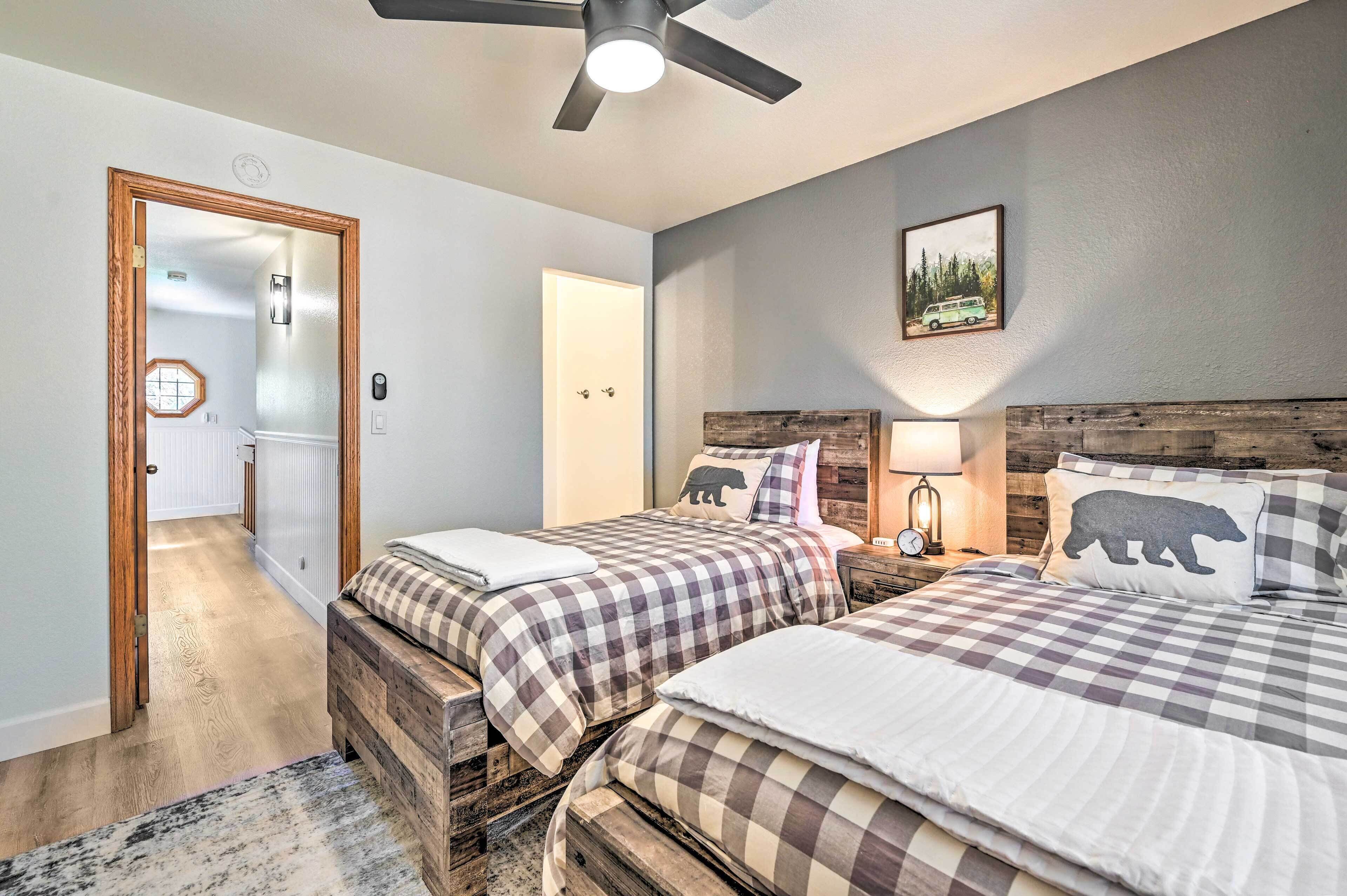 A bedroom with two beds, a ceiling fan, a nightstand with a lamp, and a door leading to another room.
