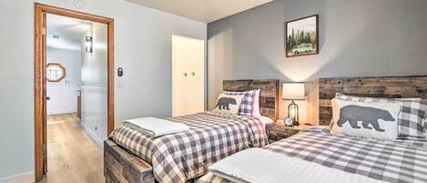 A bedroom with two beds, a ceiling fan, a nightstand with a lamp, and a door leading to another room.