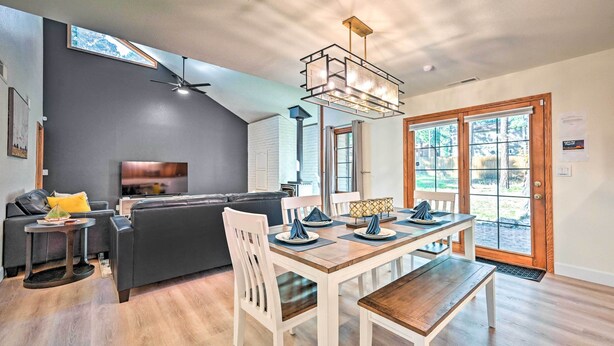 A modern living room with a dark gray wall, a black leather sofa, a wooden dining table with white chairs, and a ceiling fan. - Spacious Flagstaff Home w/ Hot Tub & Grill! (Flagstaff)