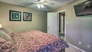 A bedroom with a bed, a ceiling fan, two framed pictures, a TV, and a door leading to a hallway. - Slopeside Condo w/ Balcony & Ski Hill Views! (Nellysford)