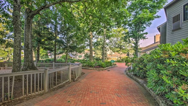 A brick pathway lined with trees and a fence, leading to a building with a light-colored exterior. - Slopeside Condo w/ Balcony & Ski Hill Views! (Nellysford)