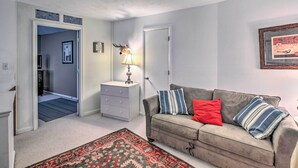 A living room with a sofa, a patterned rug, a lamp, and a door leading to another room. - Slopeside Condo w/ Balcony & Ski Hill Views! (Nellysford)