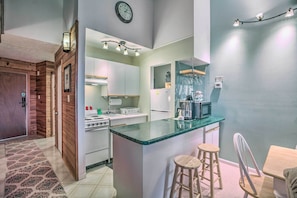 A modern kitchen with a central island, wooden accents, and a dining area with stools. - Slopeside Condo w/ Balcony & Ski Hill Views! (Nellysford)