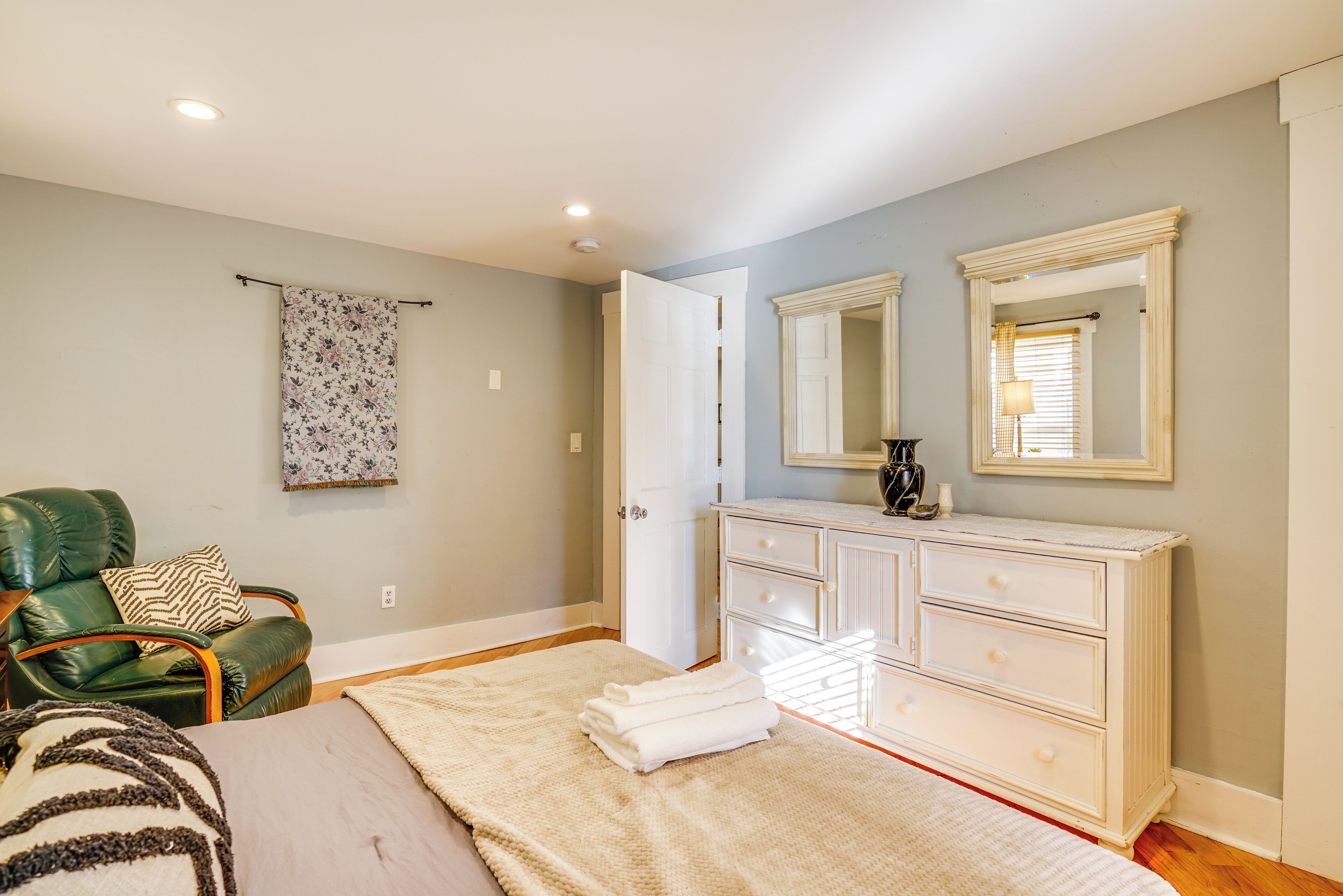Une chambre à coucher avec un lit, un fauteuil en cuir vert, une commode blanche et un miroir au mur.