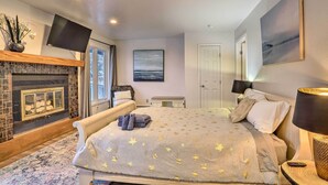A bedroom with a fireplace, a bed with a star-patterned blanket, a flat-screen TV, and a painting on the wall.