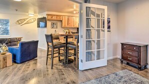 A modern living room with a blue sofa, a dining table with chairs, a wooden cabinet, and a glass door leading to a kitchen.