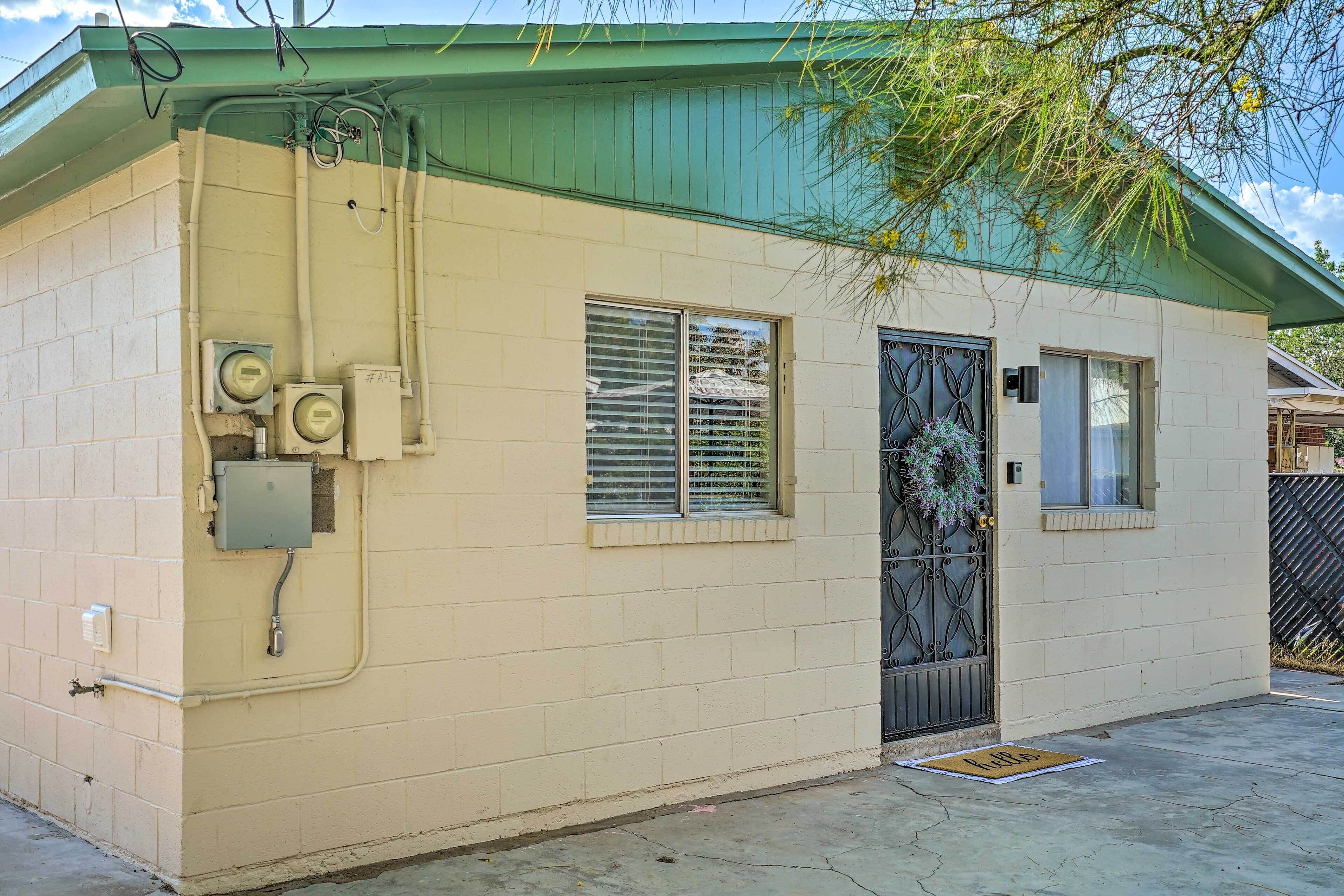 A small, single-story building with a green roof, a door with a metal gate, and a window with blinds.