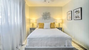 A bedroom with a large bed, two bedside lamps, a ceiling fan, and framed artwork on the wall. - El Paso Cottage - Walk to UMC & Texas Tech! (El Paso)