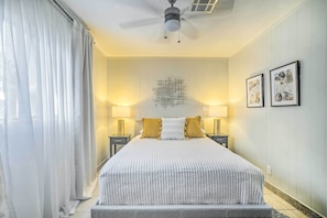 A bedroom with a large bed, two bedside lamps, a ceiling fan, and framed artwork on the wall. - El Paso Cottage - Walk to UMC & Texas Tech! (El Paso)