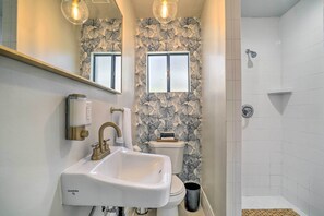 A bathroom with a white sink, a toilet, and a shower. There are two windows with frosted glass, and the walls have a leaf pattern wallpaper.