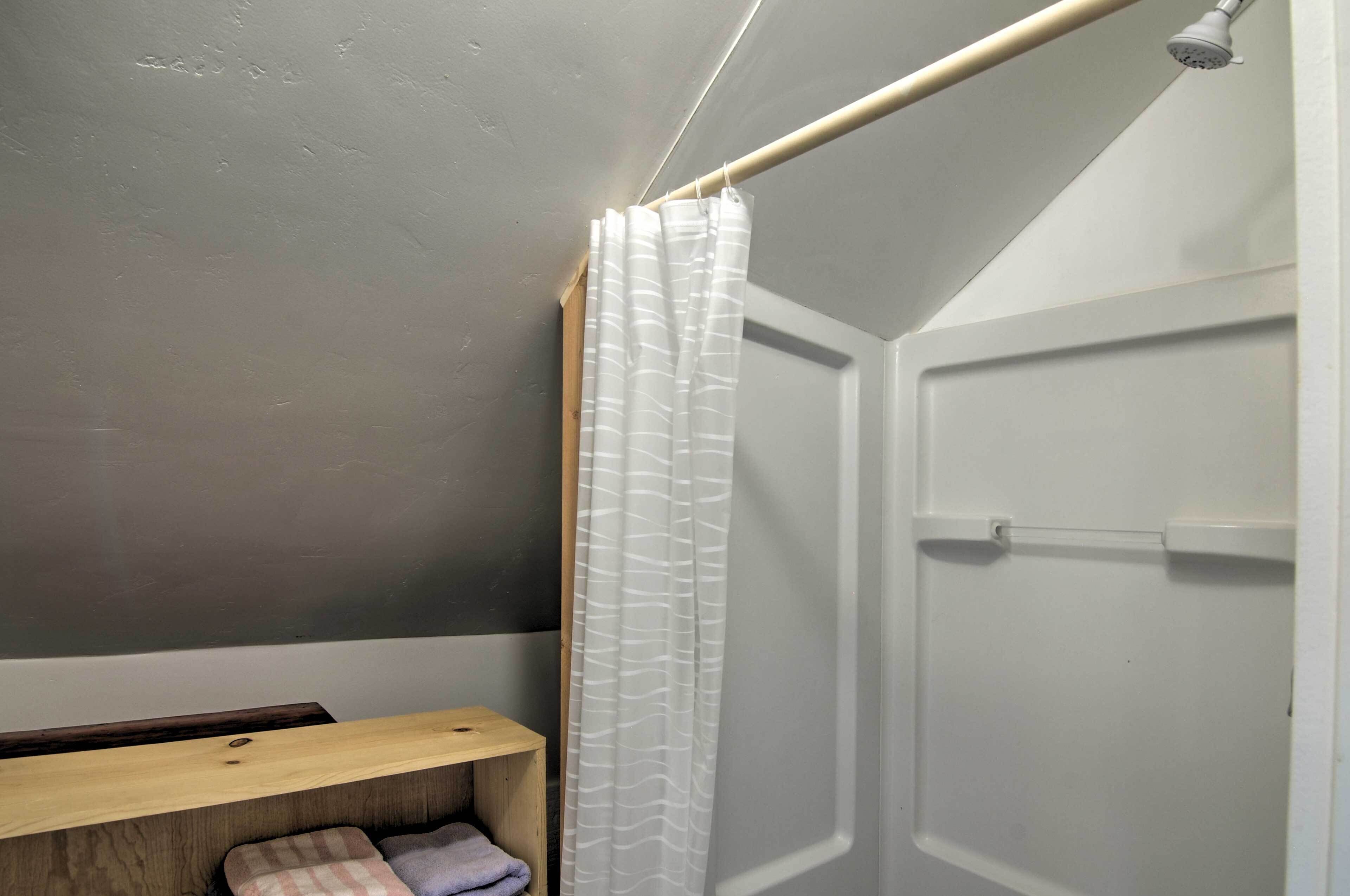A bathroom with a shower, a towel rack, and a wooden shelf.