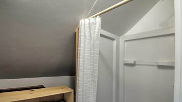 A bathroom with a shower, a towel rack, and a wooden shelf.