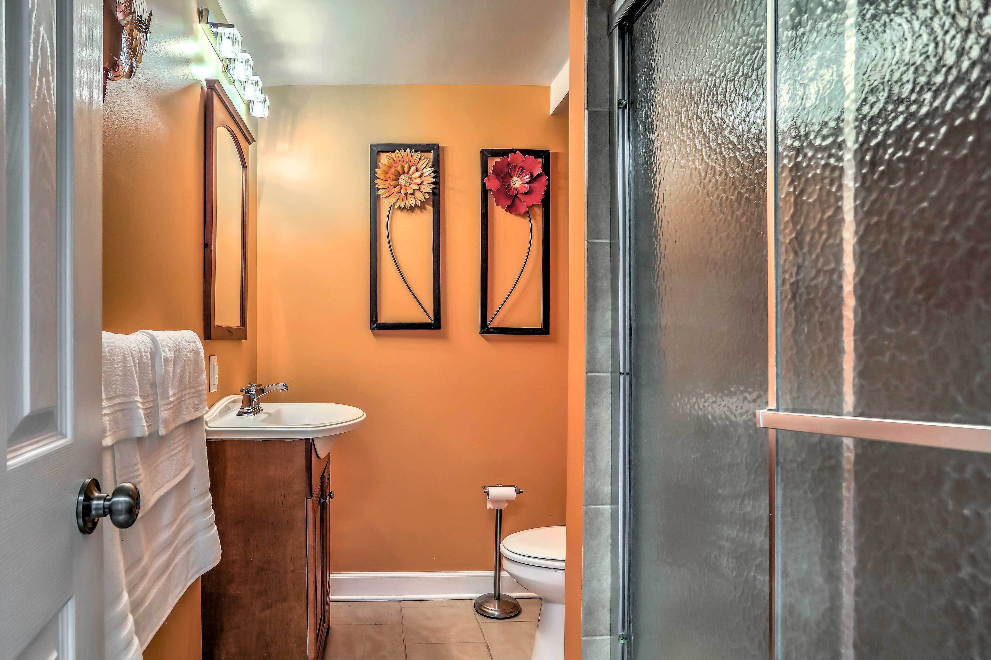 A bathroom with a white sink, a toilet, and a shower. There are two framed floral decorations on the wall.