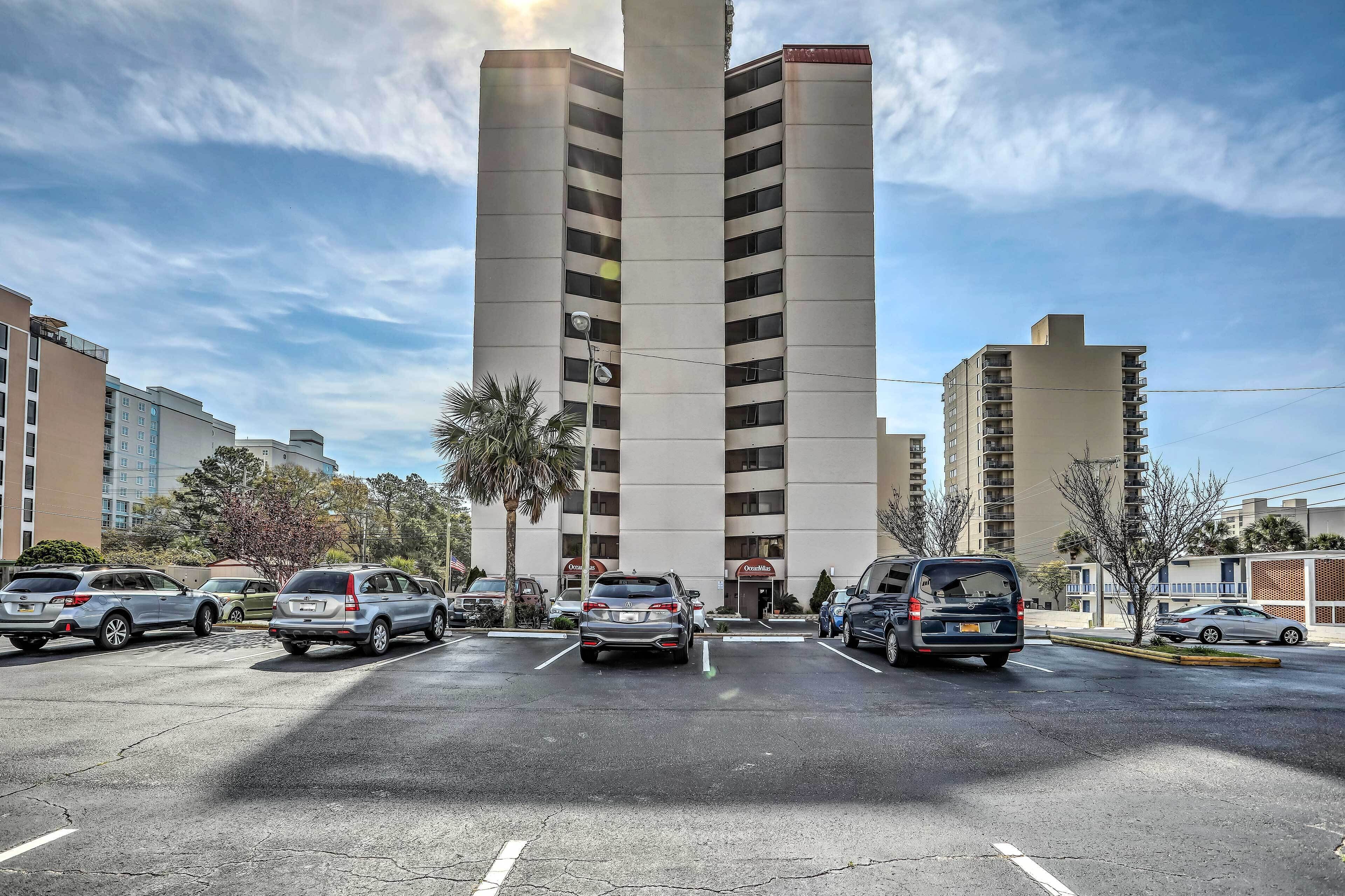 A parking lot with multiple cars, a tall building with a sign for 'Ocean Villas,' and a clear sky.