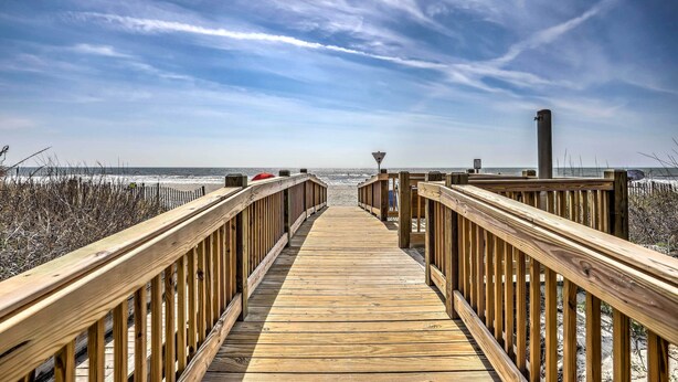 Een houten looppad dat naar een strand leidt, onder een heldere lucht.