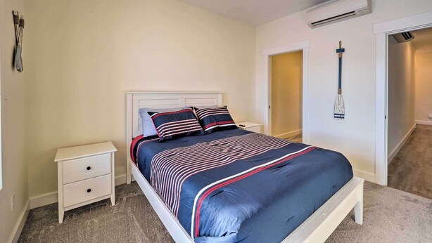 Une chambre à coucher comprenant un lit, une table de chevet, un climatiseur fixé au mur et une porte donnant sur une autre pièce.