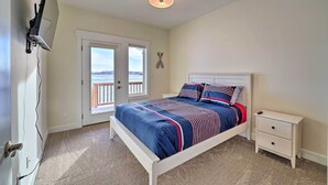 Une chambre à coucher comprenant un lit, une table de chevet, un téléviseur fixé au mur et une porte donnant sur un balcon.