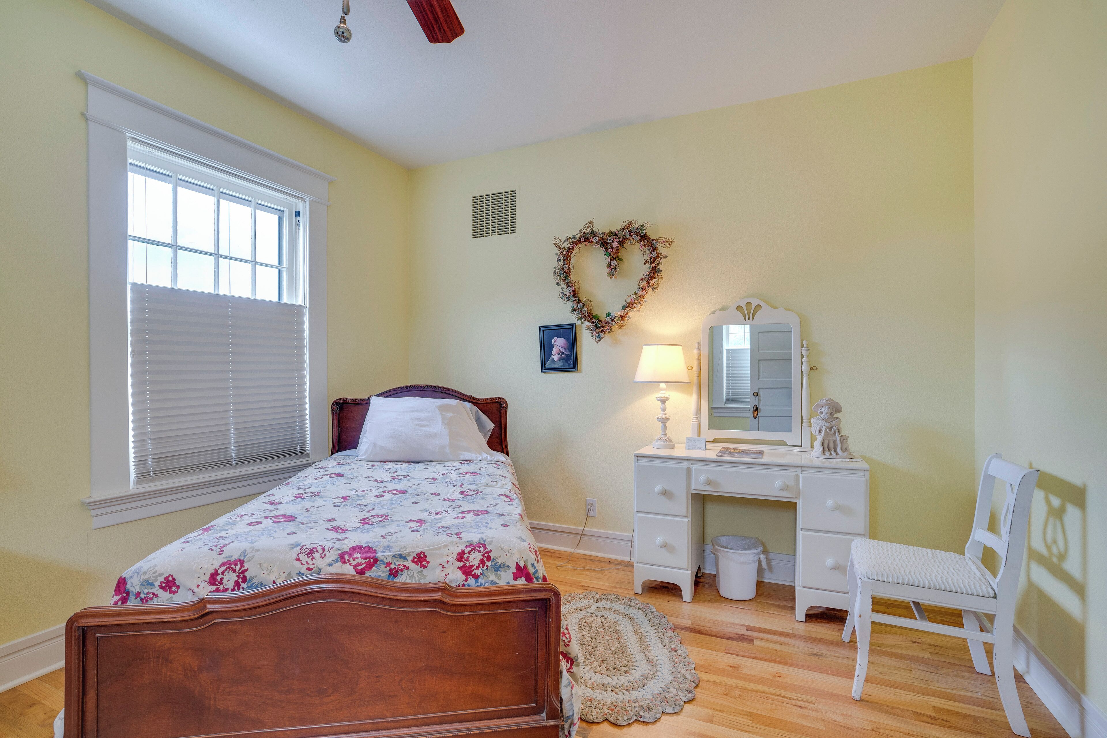 A bedroom with a bed, dresser, chair, and a heart-shaped decoration on the wall.