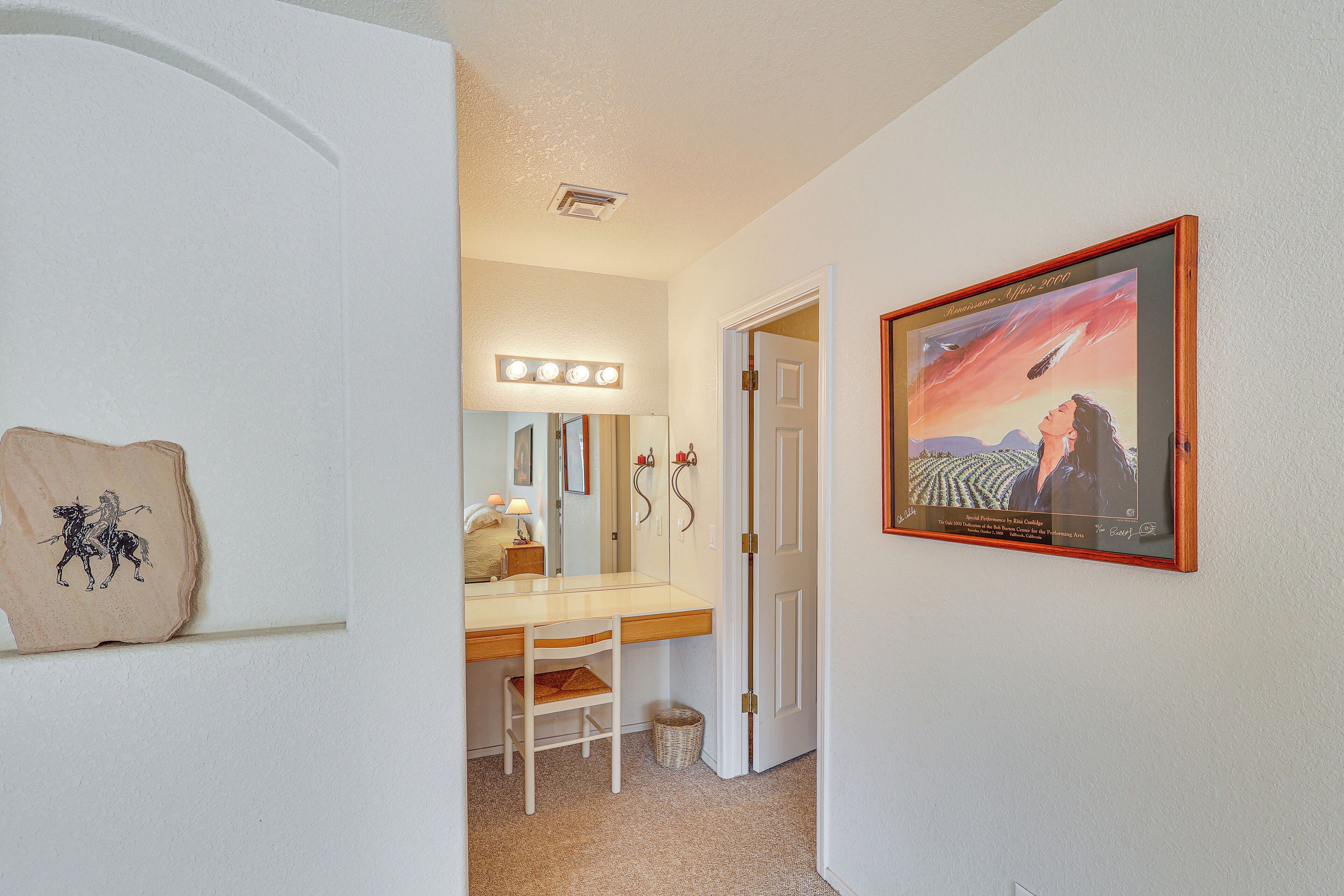 A hallway with a vanity mirror, a framed picture, and a door leading to another room.