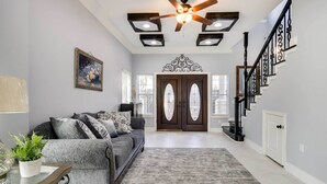 A living room with a gray sofa, a glass coffee table, and a ceiling fan. - Luxe Southwest Houston Home w/ Balconies & Patio! (Houston)