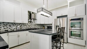 A modern kitchen with white cabinetry, a black countertop island, stainless steel appliances, and a tiled backsplash. - Luxe Southwest Houston Home w/ Balconies & Patio! (Houston)