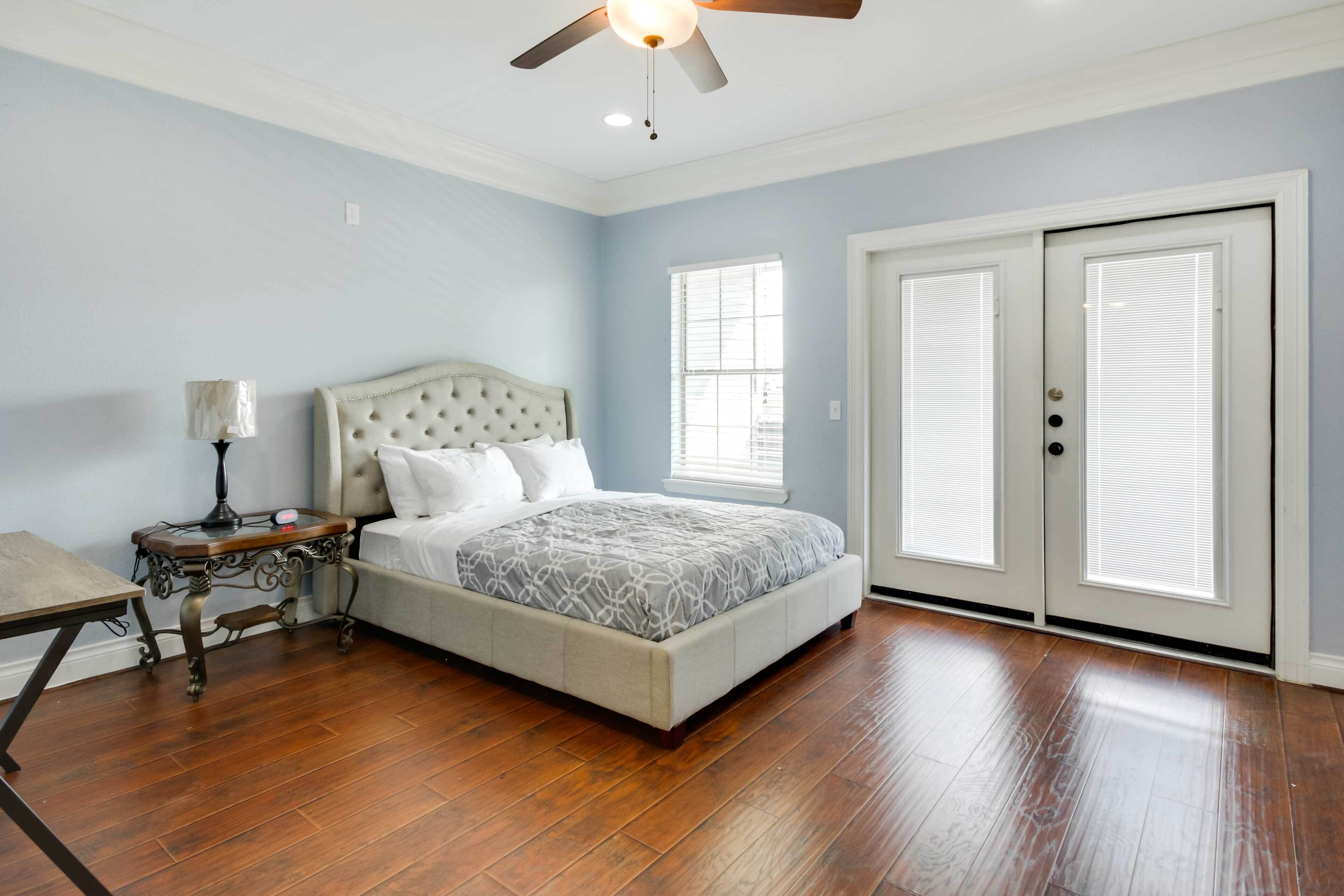 A bedroom with a bed, a nightstand, a lamp, a ceiling fan, and a door with blinds.