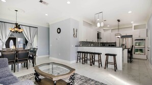 A spacious living area with a glass coffee table, a dining set, and a kitchen with modern appliances and bar stools. - Luxe Southwest Houston Home w/ Balconies & Patio! (Houston)
