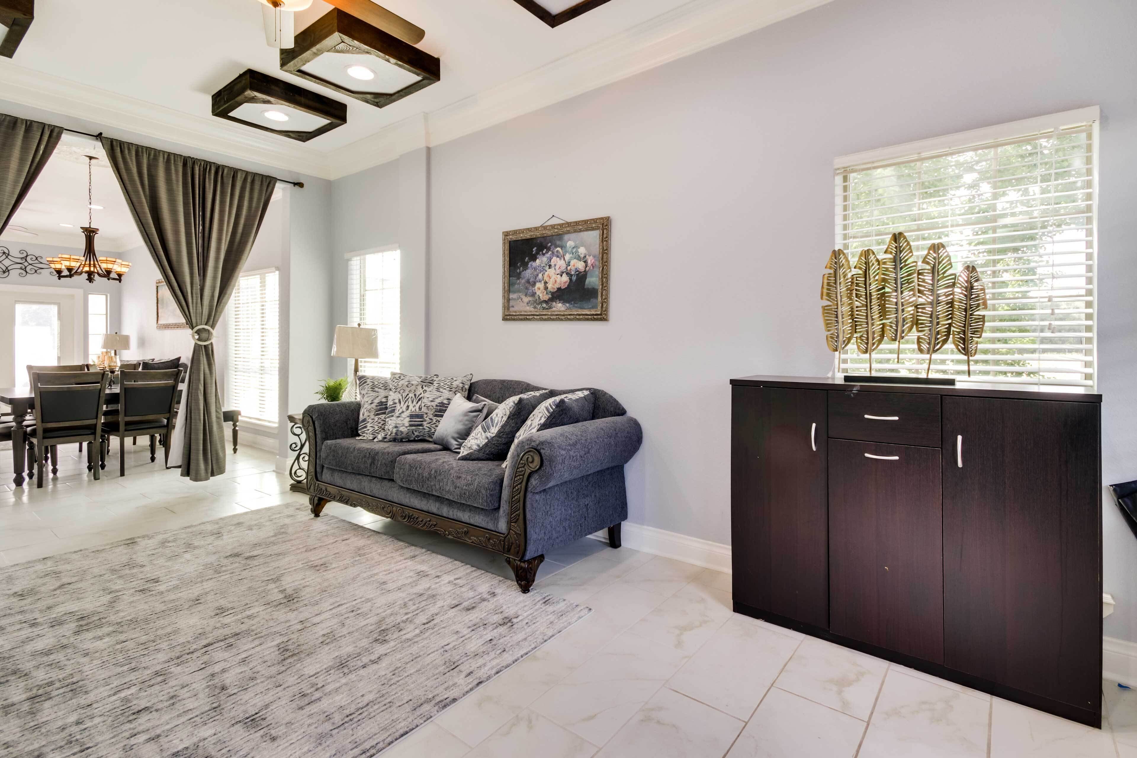 A spacious living room with a grey sofa, dark wooden cabinet, and a dining area with a chandelier.