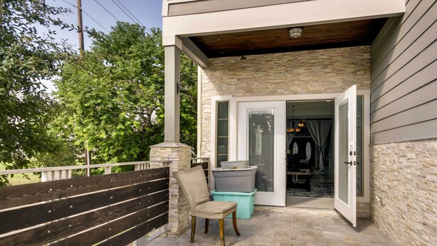 A covered outdoor area with a stone wall, a bench, and a door leading to an interior space. - Luxe Southwest Houston Home w/ Balconies & Patio! (Houston)