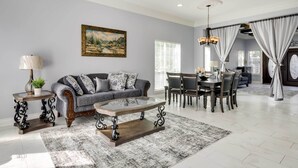 A spacious living room with a gray sofa, a glass coffee table, and a dining area with a wooden table and chairs. - Luxe Southwest Houston Home w/ Balconies & Patio! (Houston)